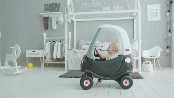 Joyful Infant Girl Sitting in Baby Car at Home