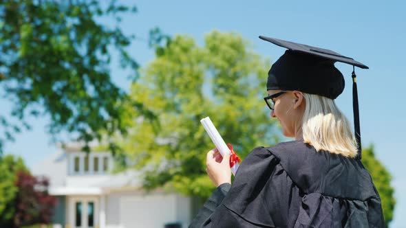 Student Graduate in Mantle and Cap Against the Background of His House