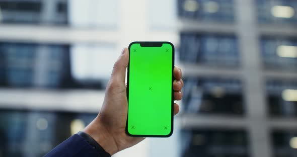A Man's Hand in a Business Suit Holds a Mobile Phone with a Green Screen