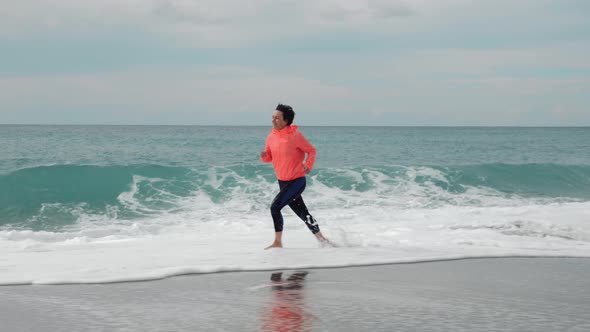 Woman is running in surf waves on empty sandy beach 