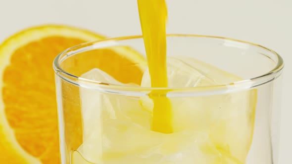 Pouring Orange Soft Drink Into Glass with Ice Cubes