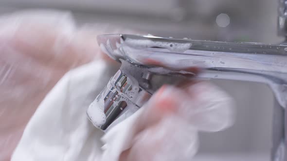 Woman's Gloved Hand Cleans a Stainless Steel Water Tap in the Bathroom with Detergent. Hygiene in