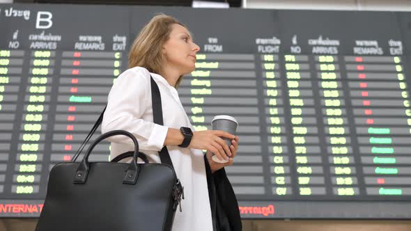 Young Business Woman With Coffee Waiting At Airport Flight Departure Screen