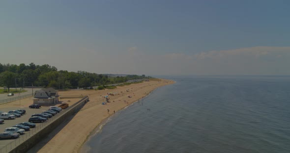 Backwards Aerial Pan Zooming Out from Beach Shore Near Forest and Parking Lot