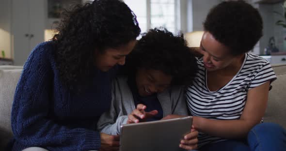 Mixed race lesbian couple and daughter using digital tablet on couch laughing