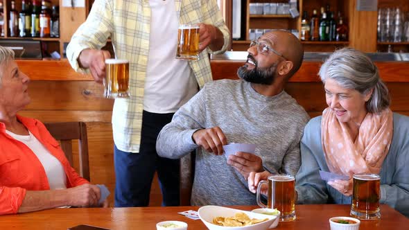 Happy friends playing cards while having glass of beer 