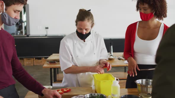 Caucasian female chef teaching diverse group wearing face masks