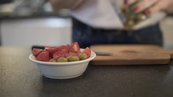 Handheld Shot of Woman Adding Olives To the Salad with Tomatoes