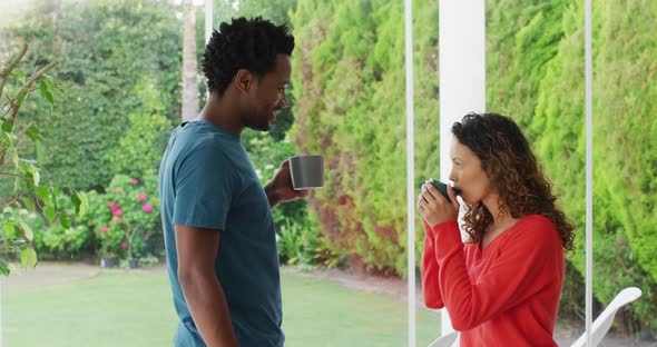 Happy biracial couple relaxing and drinking coffee together on patio