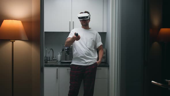 Man at Home Put on Vr Goggles and Use Remote Controller Standing in Kitchen