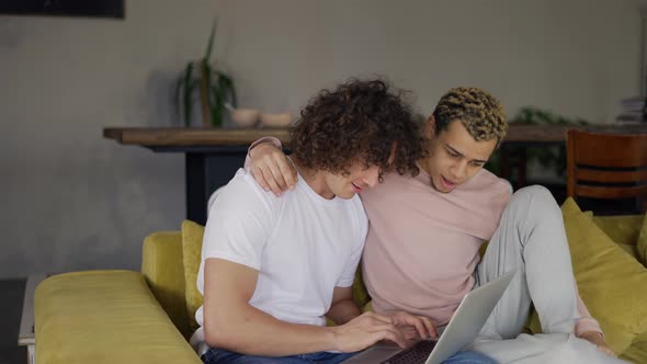 Two Male Gay Couple Embraced Using Laptop Surfing Internet Together for Fun