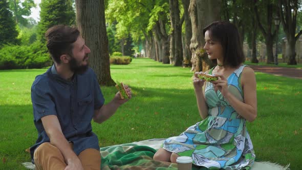 Young Couple in Summer Picnic Park To Eat Sandwiches, Enjoying the Flavor and Smiling