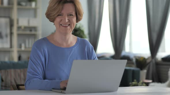 Smiling Old Senior Woman Looking at Camera while Working on Laptop