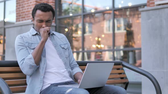 African Man Coughing while Working on Laptop Outdoor