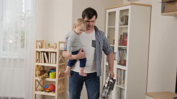 Young father holding his baby son while doing house cleanup