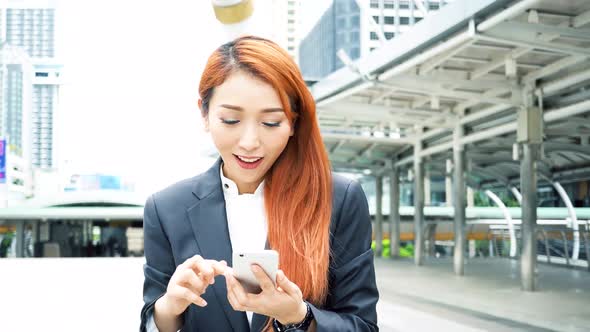 Young Attractive Asian Using Mobile Phone and Walking with Smile Over High Rise Building Background