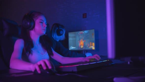 Two Pretty Gamer Girls Playing an Online Shooter Game in the Neon Gaming Club