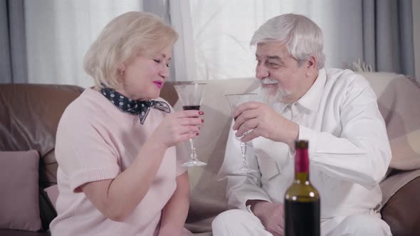 Camera Approaching To Old Married Caucasian Couple Clinking Glasses and Drinking Wine, Cheerful