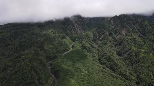 Aerial view of flying in a tropical forest, mountain, and valley in Indonesia.