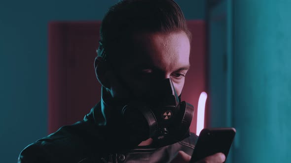 Portrait of Dangerous Man in Respirator Using Smartphone at Night Over Neon Lights. Cyberpunk