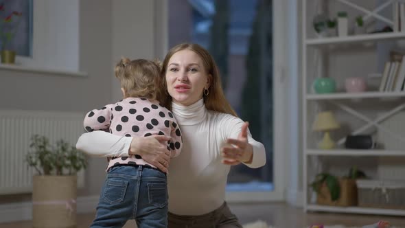 Medium Shot of Smiling Gorgeous Millennial Mother Hugging Baby Daughter Talking