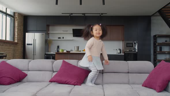 Excited Cute Asian Toddler Girl Jumping on Sofa