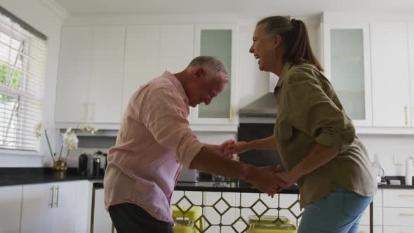 Caucasian senior couple dancing together in the kitchen at home