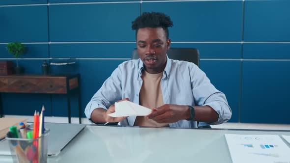 African American Man Having Fun in Office Folded Paper Into Plane and Launching
