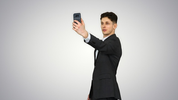 Young business man walking and taking a selfie on gradient