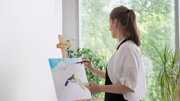 Mature Woman Paints Sky on Canvas with Paintbrush Closeup