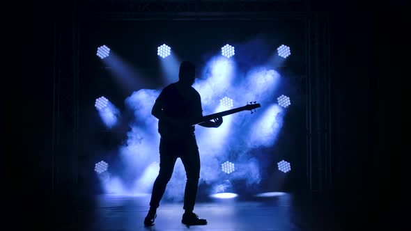 Silhouette of a Young Guy Playing on the Electric Guitar on Stage in a Dark Studio with Smoke and
