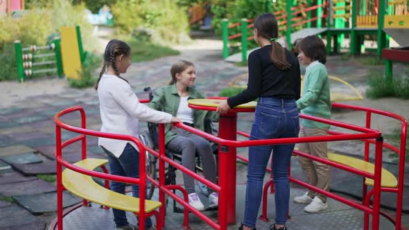 Group of Caucasian Children Enjoying Leisure on Playground with Friend in Wheelchair