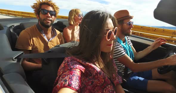 Attractive young people enjoying music while driving in convertible