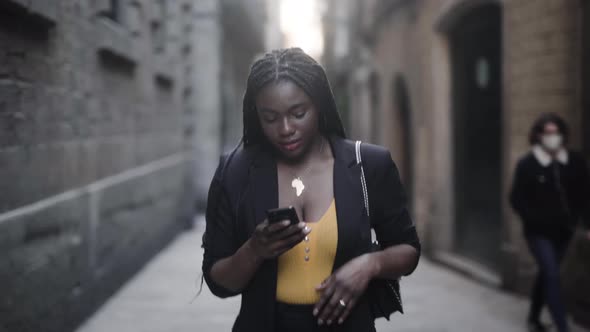 Smiling black woman speaking on smartphone while walking on street