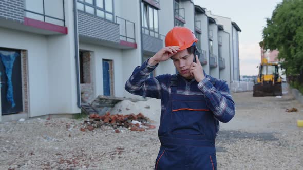 Man Speaks on His Phone and Holds Helmet