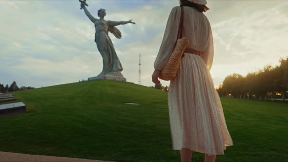 A young girl in a dress looking at Mother Motherland at sunset