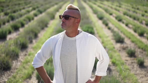 Medium Shot Portrait of Satisfied Gardener Standing on Lavender Field Holding Hands on Hips Looking