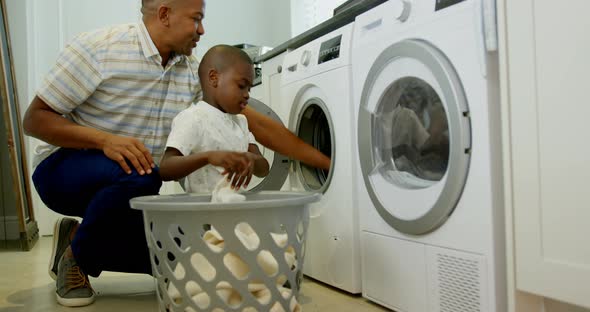 Side view of mid adult black father and son washing clothes in washing machine at comfortable home 4