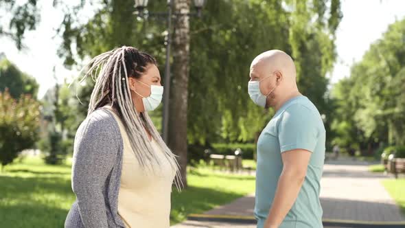 Two Happy Friends in Medical Mask Keep Social Distance Sitting and Talking Outside on Bench in Park