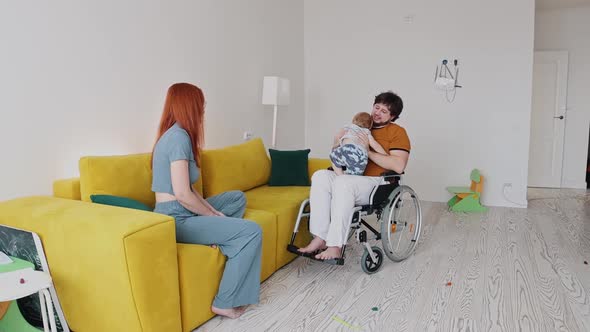 A Man in a Wheelchair Playing with His Baby Son and His Wife Watching Them