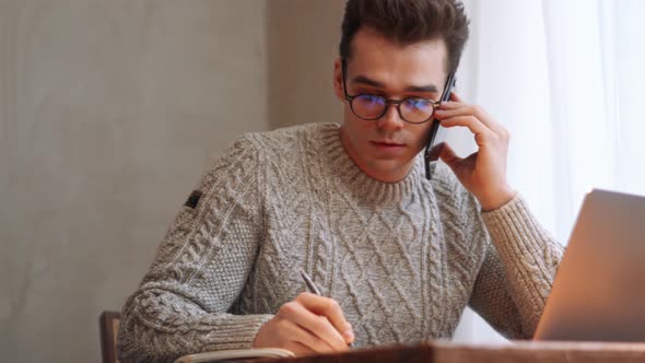 Smiling man wearing eyeglasses writing something and talking on phone