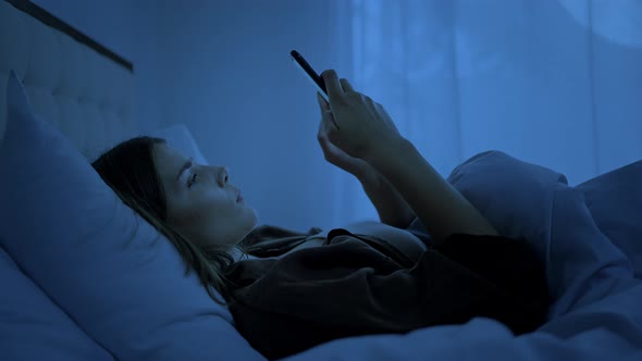 Frustrated Woman Lies on Bed Sending Messages to Friend