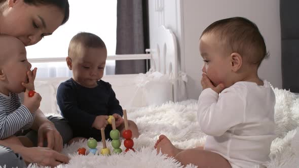 Teething Asian Triplets Putting Stacking Toy Beads in Mouth