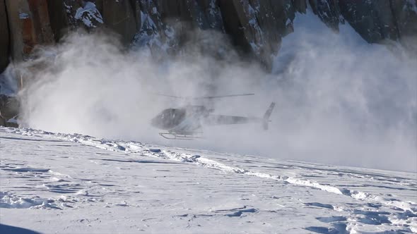 A helicopter landing on snow for skiing in the mountains.