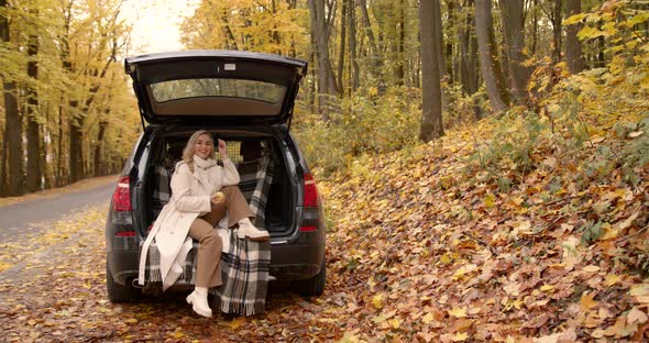 Woman in a Beige Coat Sitting in the Trunk of a Car