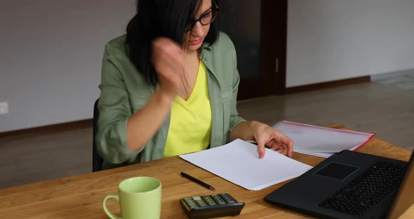 Stylish brunette woman in glasses sitting at wooden table with notepad working in her office