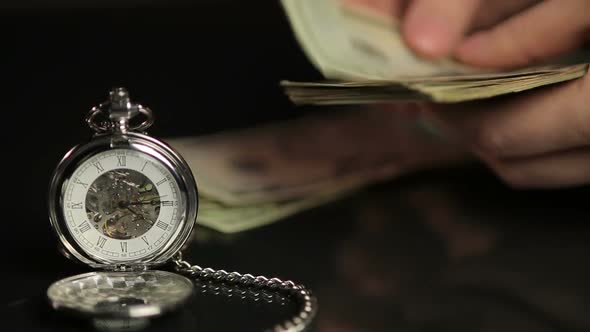 Person Counting Dollar Bills, Summing Up Investment Results, Watch Showing Time