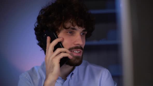 Close-up of young man talking on mobile phone and using computer working at home doing distant work.