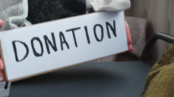 Female Volunteer Making Donation Box with Old Used Clothes Indoors