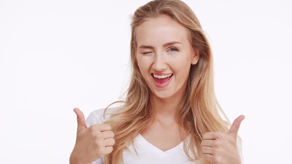 Young Beautiful Caucasian Blonde Girl Smiling at Camera and Showing Ok with Two Thumbs on White